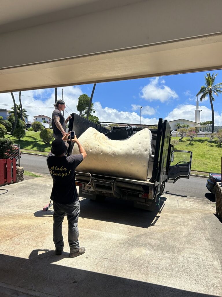 Aloha Junk Man workers loading a large mattress onto a junk removal truck at a customer's property in Kailua, HI.