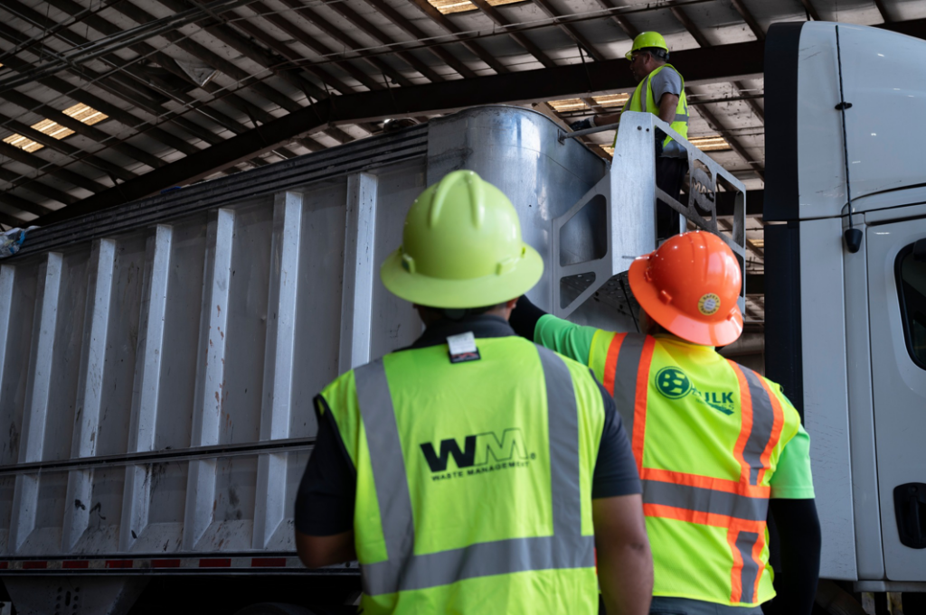 Workers in safety vests and hard hats loading waste onto a large truck for Bulk Environmental and Industrial in Miami, FL