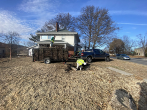 Two workers from Harris Family Hauling & Snow Removal LLC loading yard debris into a trailer in Independence, MO.