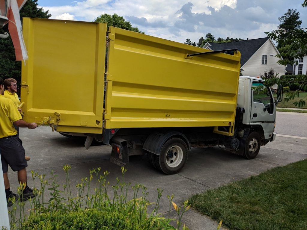 Workers in yellow shirts loading a yellow dump truck, demonstrating junk removal services by Junk Solutions in Ogden, UT.