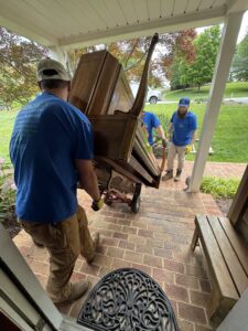 Two workers from Barkers Junk Removal & Hauling LLC moving a large wooden dresser with a dolly in Roanoke, VA.