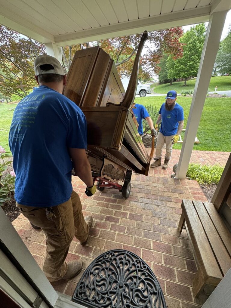 Two workers from Barkers Junk Removal & Hauling LLC moving a large wooden dresser with a dolly in Roanoke, VA.