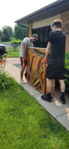 Two workers from 402 Junk Removal in Lincoln, NE, carefully moving a heavy piano or large piece of furniture with straps.