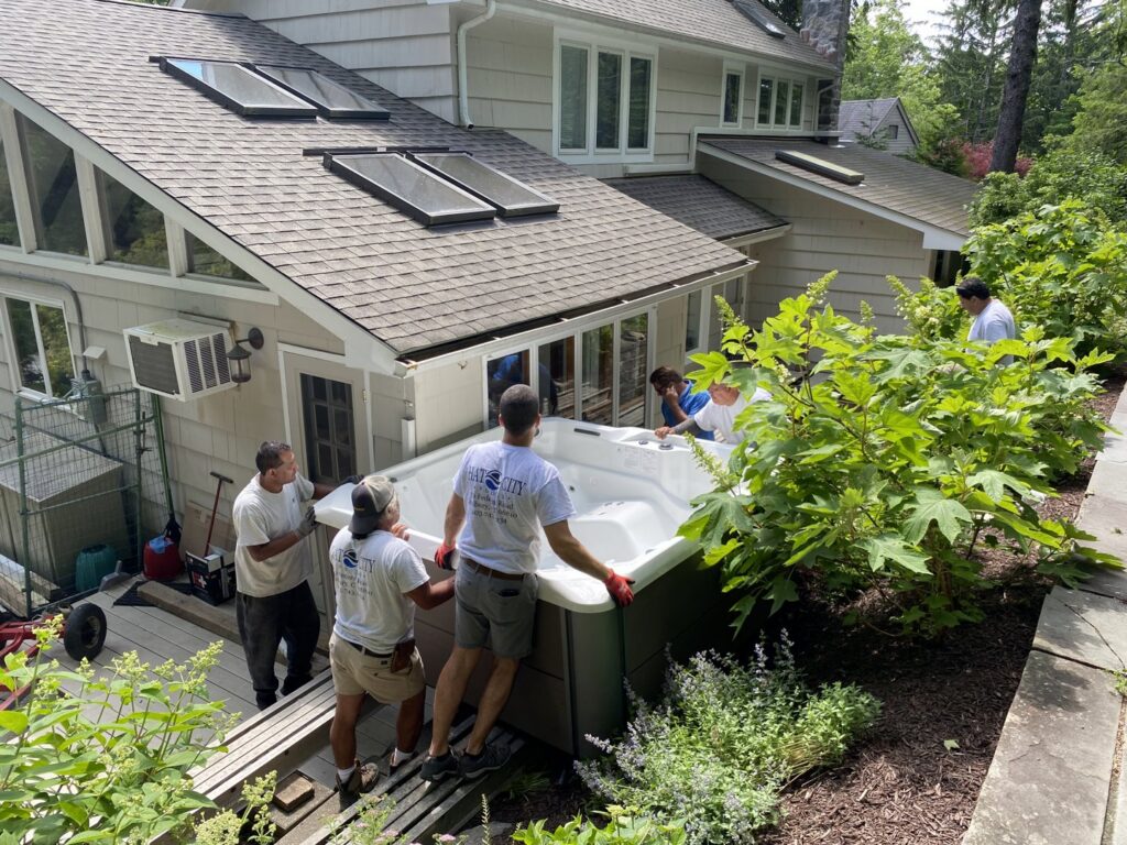 Workers from Hat City Pools carefully moving a new hot tub onto a residential deck in Danbury, CT