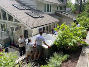 Workers from Hat City Pools carefully moving a new hot tub onto a residential deck in Danbury, CT