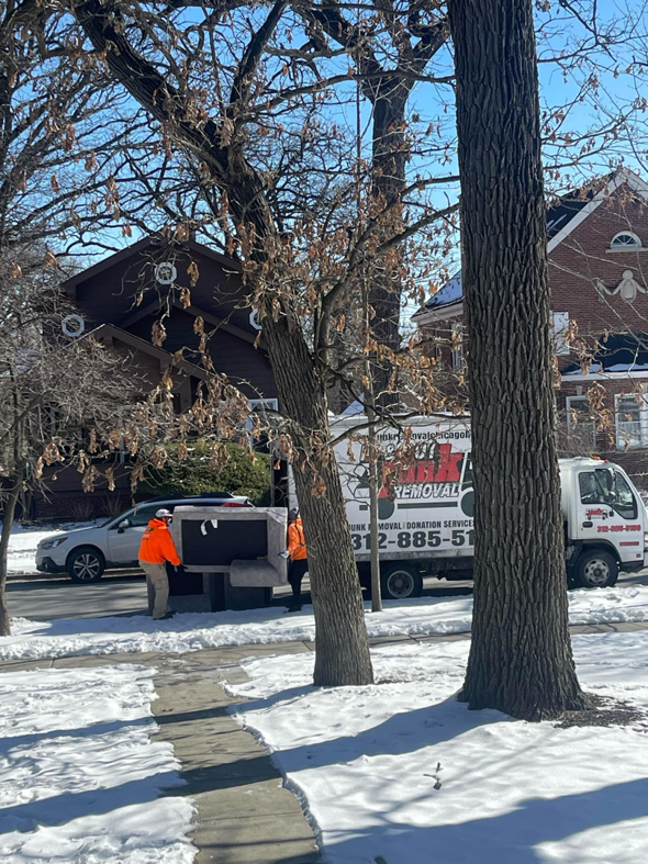 Two workers moving a large piece of junk towards a removal truck for In & Out Junk Removal Service LLC in Chicago, IL.