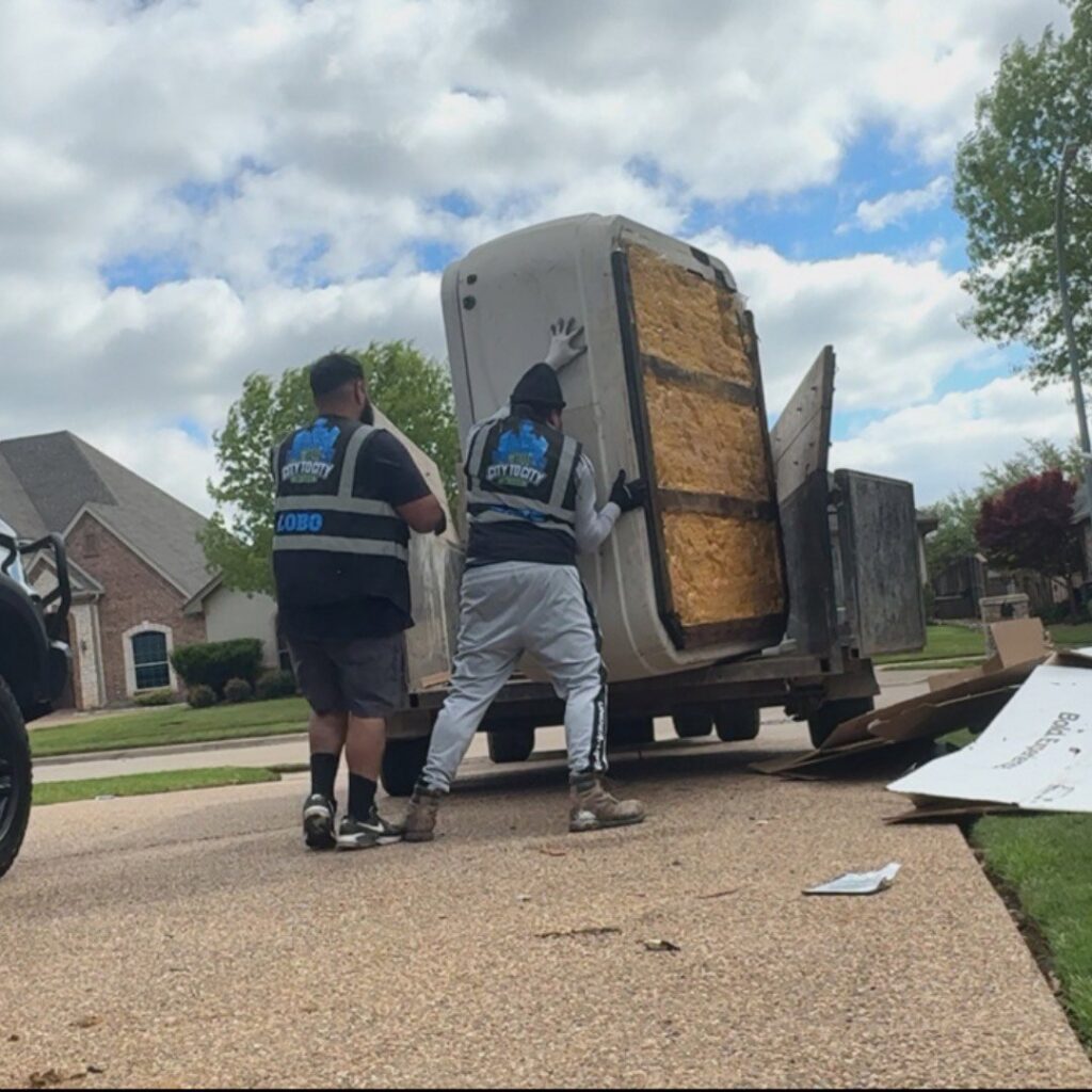 Two City to City Junk Removal Fort Worth, TX workers carefully moving a large, heavy item onto a trailer during a junk removal job.