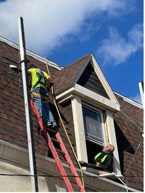 Construction workers on a ladder and in a window performing roof work for RHI Construction Inc in Philadelphia, PA.