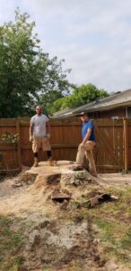Two workers standing on a large tree stump with sawdust, indicating stump grinding or removal by Clyde's Tree Service in Indianapolis, IN.
