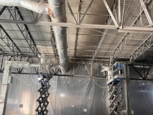 Workers on scissor lifts spraying paint or coating on ceiling structures and ductwork for Bell SPI - Shamrock Painting in Denver, CO.