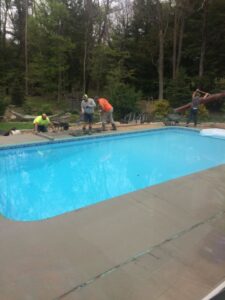 Workers pouring and leveling concrete for a new pool deck around an inground pool by My Pool Guys of Erie, PA.