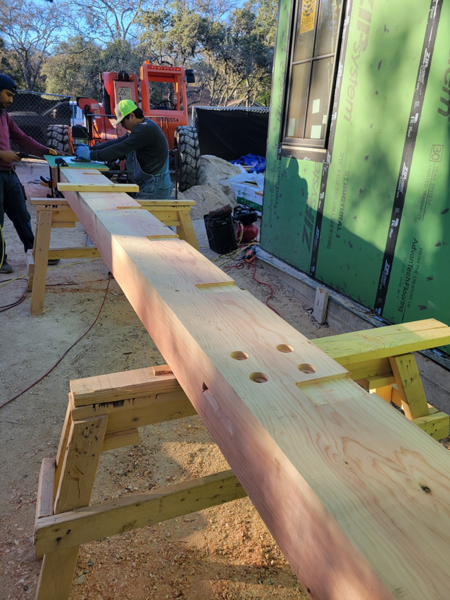 Workers preparing a large wooden beam for construction at a job site by Hill Country Framing in Austin, TX