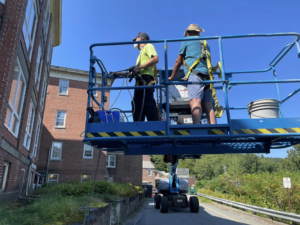 Two workers on a boom lift pressure washing a building exterior for Infinity Maintenance Services, Inc. in Brattleboro, VT.