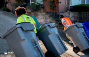 Two Bay Area Bin Support workers pushing multiple residential waste bins up a street in San Leandro, CA.