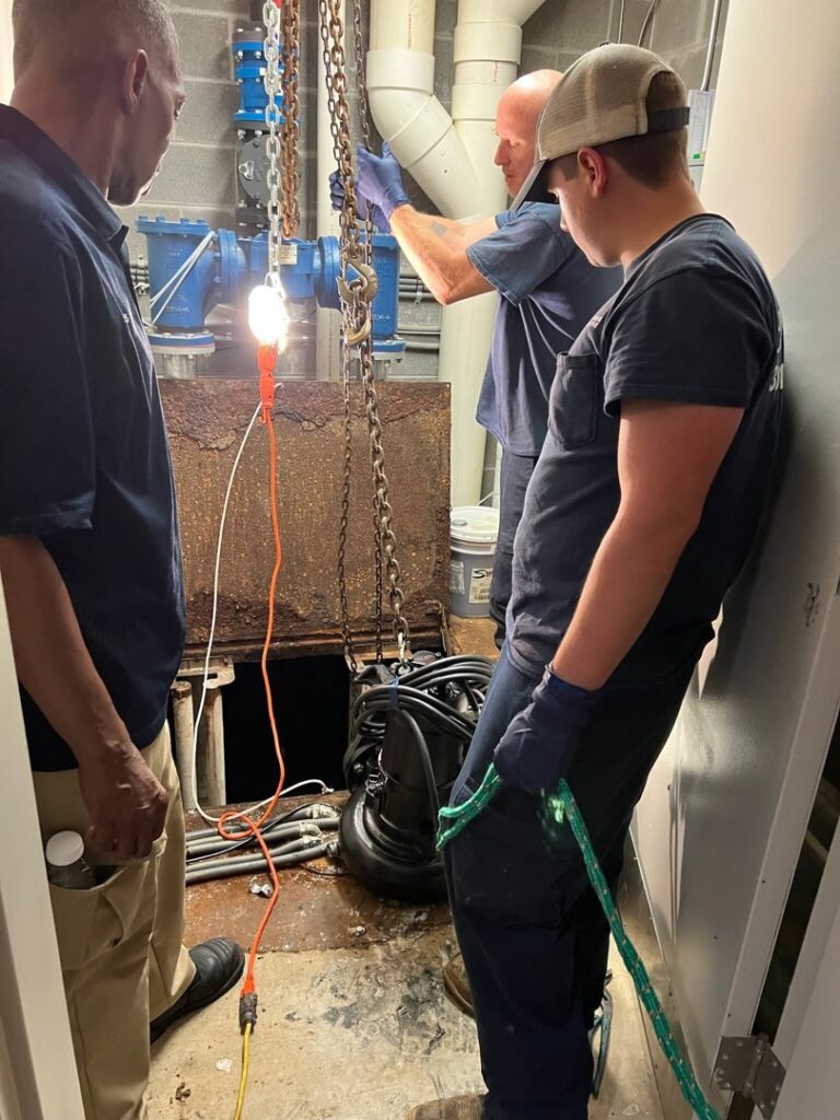 Workers from JF Plumbing & Heating removing a large pump from a pit during a service in Rockville, MD.