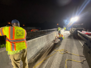 Workers in safety vests repairing a bridge barrier at night, a handyman service provided by Memphis Fence Company, LLC in Memphis, TN.