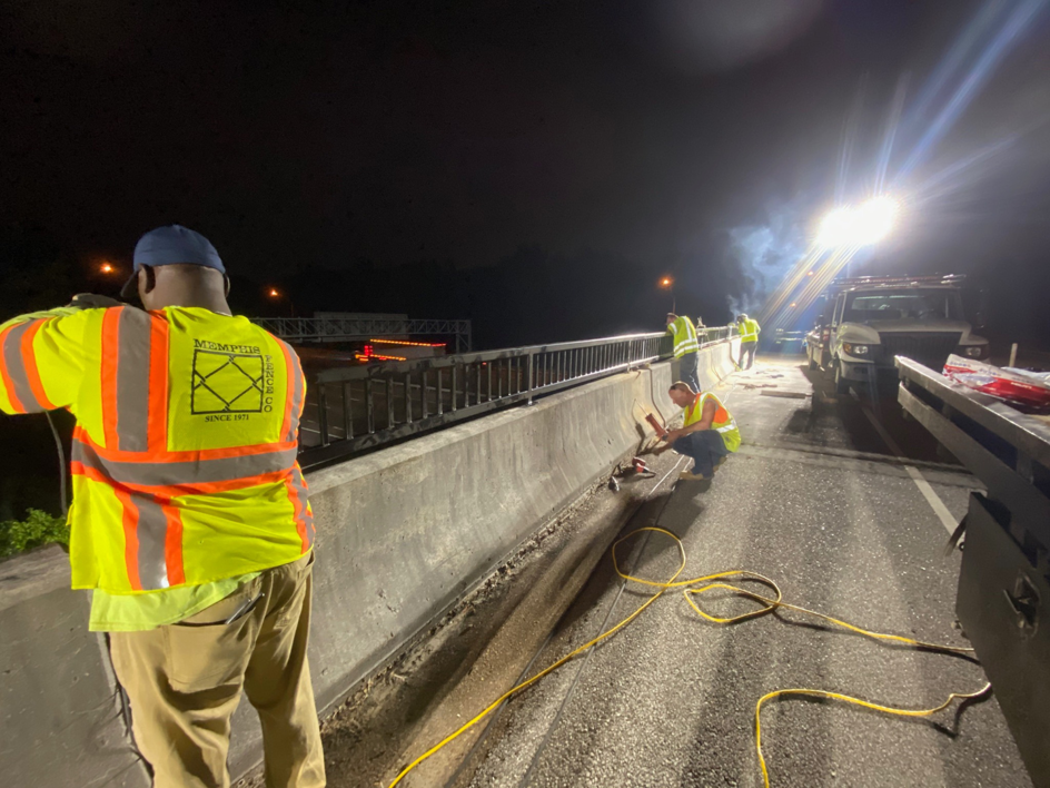 Workers in safety vests repairing a bridge barrier at night, a handyman service provided by Memphis Fence Company, LLC in Memphis, TN.