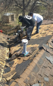 Two workers actively repairing a severely damaged roof, removing old shingles for RRC Reign Roofing & Construction in Oklahoma City, OK.