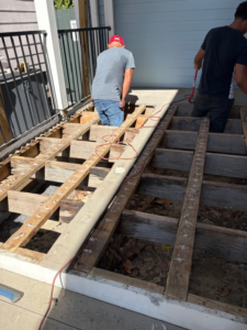 Two workers repairing the wooden deck framing of a porch in New Orleans, LA, by Richard Earls Construction.