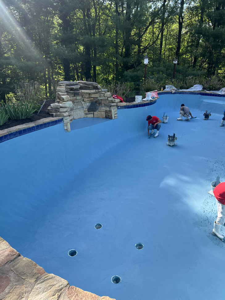 Workers applying a fresh blue coating to the interior of a pool during a resurfacing job by Sublime Pools RVA in Richmond, VA.