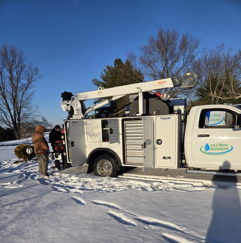 Two workers next to a service truck with a crane in a snowy environment for S & L Water Solutions in Hagerstown, MD.
