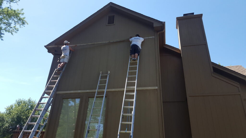 Two workers on ladders performing siding and trim repair or installation on a house exterior for E.L. Construction in Kansas City, MO.
