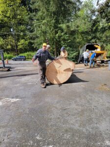 Workers from Haskins Tree Care in Bellevue, WA, handling a large tree trunk section with a wood chipper in the background.