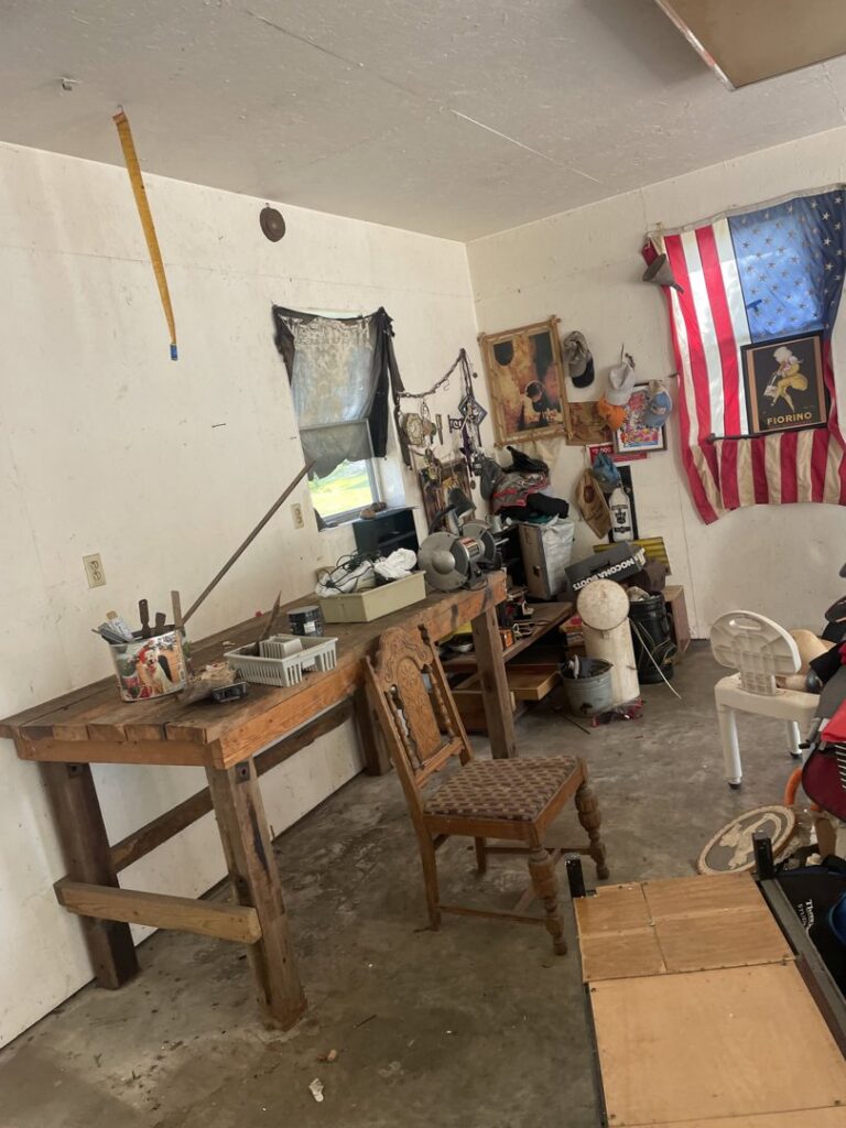 A cluttered workshop with tools, a workbench, and various items, indicating a cleanout service by DC'S Removal Service in Neelyville, MO.