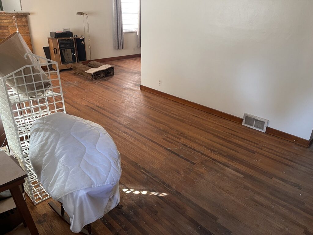 A room with worn hardwood floors before refinishing, showing the initial state for NV Floors LLC in Pittsburgh, PA.