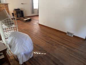 A room with worn hardwood floors before refinishing, showing the initial state for NV Floors LLC in Pittsburgh, PA.