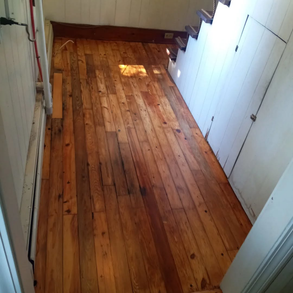 A worn, old wood floor in a hallway before refinishing by Robert C. Mihaich Wood Flooring in Worcester, MA.