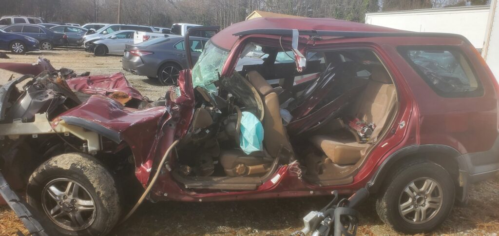 A completely wrecked red SUV, seen from the side, awaiting junk car removal by Don's Automotive Removal in Thomasville, NC.