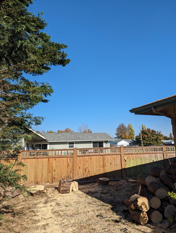 A residential yard showing tree stumps, wood chips, and a pile of logs after tree removal by Yost Tree Service in Salem, OR.