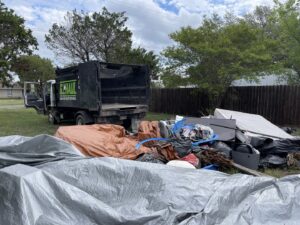 A large pile of yard debris and household junk, with a G.I. HAUL Austin, TX truck parked nearby for removal.