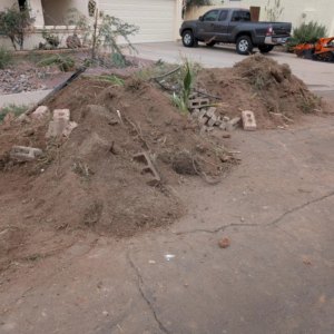 Large piles of dirt, yard waste, and construction debris on a driveway, awaiting removal by All-Pro HAUL Property Services in Phoenix, AZ.