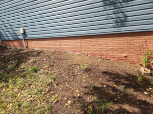 The area next to a house after yard waste and brush removal by 402 Junk Removal in Lincoln, NE, showing a clean, cleared space.