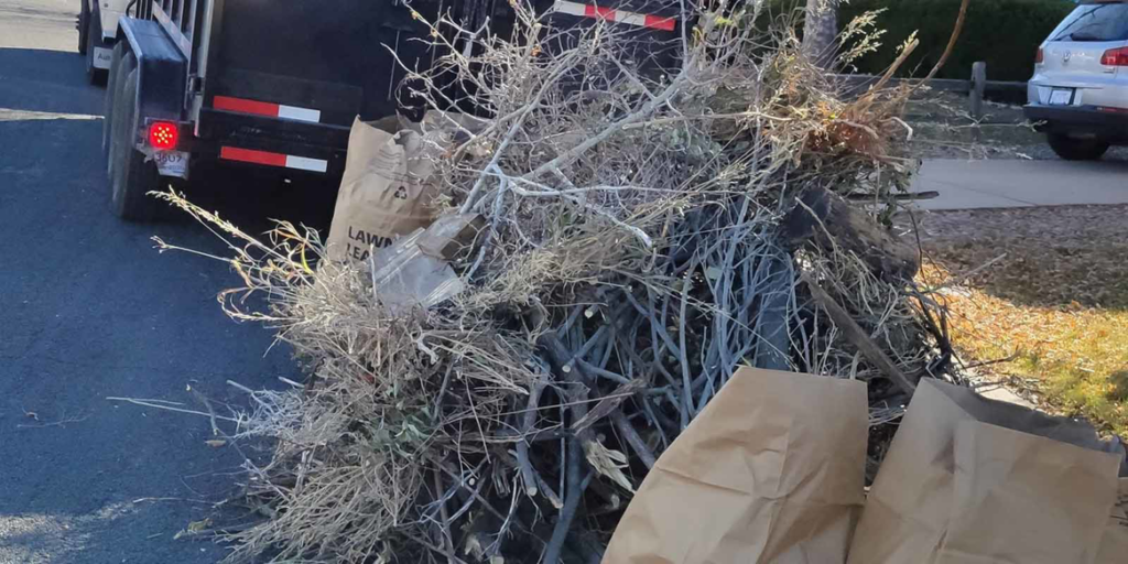 A large pile of yard waste and brush next to a junk removal trailer by Super Junkers in Denver, CO