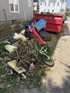 A large pile of yard waste, old furniture, a bicycle, and trash next to a red dumpster, handled by Junk Removal Brothers in Worcester, MA.