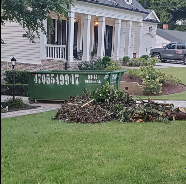 A large pile of yard waste and branches next to an IEG Disposal roll-off dumpster for removal in Canton, GA.