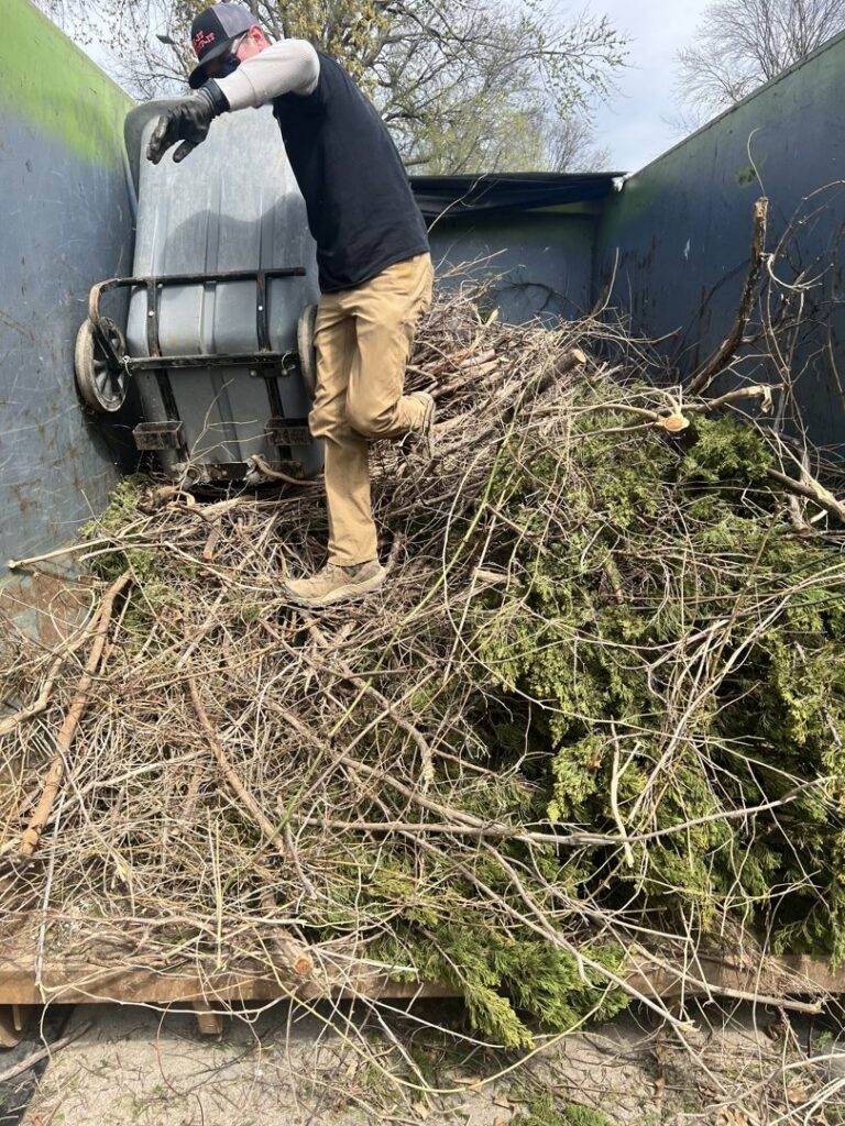A Junk It OR Dump It worker in Independence, MO, loading yard waste and branches into a junk removal truck.