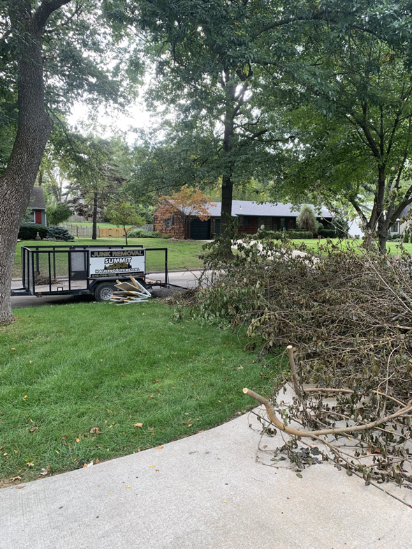 A Summit Hauling & Removal trailer parked next to a large pile of yard waste, ready for pickup in Lee's Summit, MO.