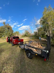 A red pickup truck pulling a trailer loaded with tree branches and yard waste for removal by L.P.Z Trash & Junk Removal in Tallahassee, FL.