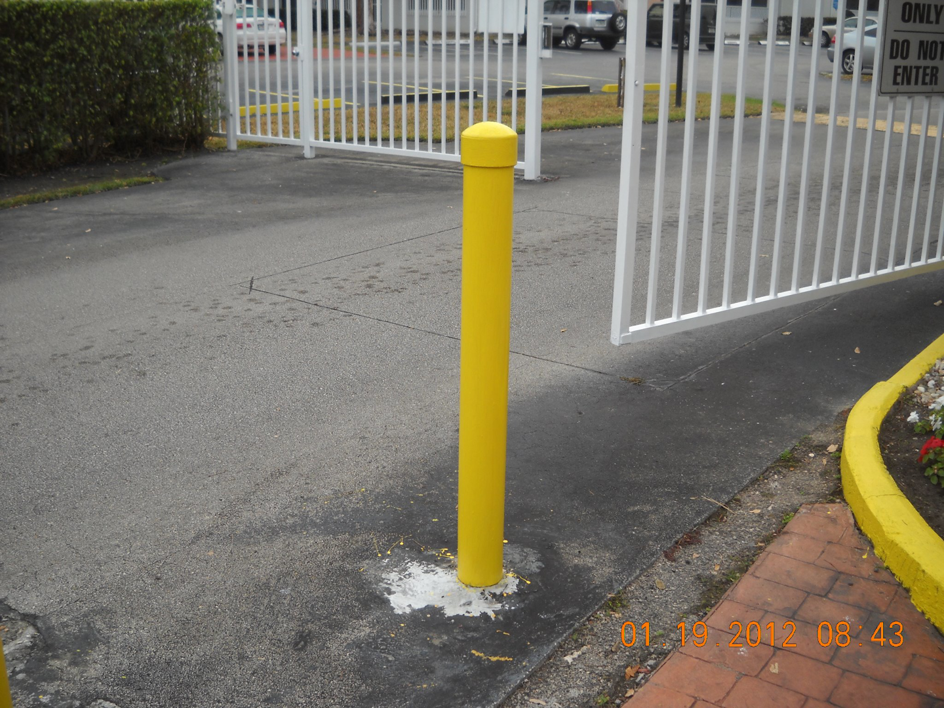 A newly installed yellow bollard next to a white gate, completed by Lee Goldstein Construction, Inc in Miami, FL