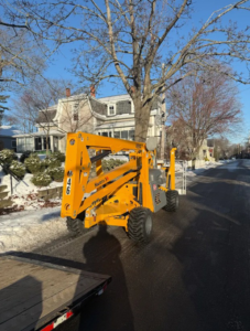 A yellow boom lift parked on a residential street, available for rent from Handyman Rental in Portland, ME.