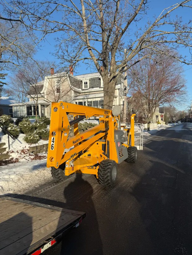 A yellow boom lift parked on a residential street, available for rent from Handyman Rental in Portland, ME.