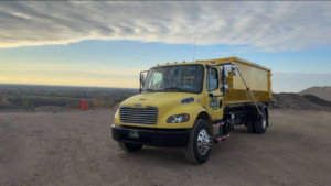 A bright yellow disposal truck with a roll-off dumpster body, used for junk removal services by Mac's Disposal LLC in Kenosha, WI.