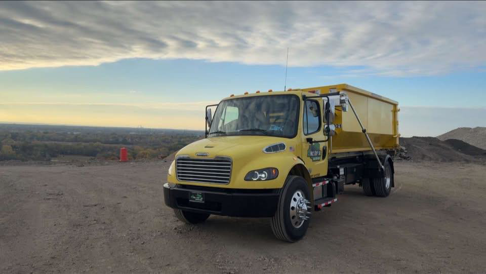 A bright yellow disposal truck with a roll-off dumpster body, used for junk removal services by Mac's Disposal LLC in Kenosha, WI.