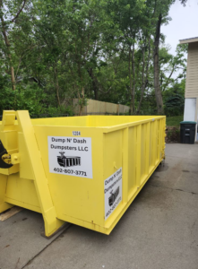 A bright yellow dumpster from Dump N Dash Dumpsters LLC parked on a residential driveway in Valley, NE, ready for junk removal.