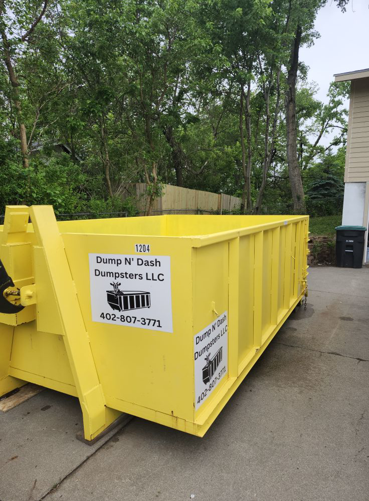 A bright yellow dumpster from Dump N Dash Dumpsters LLC parked on a residential driveway in Valley, NE, ready for junk removal.