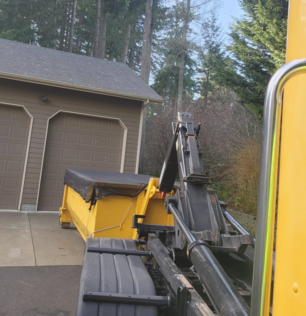 A yellow roll-off dumpster with a tarp being loaded onto a truck by ADE Hauling in Tacoma, WA